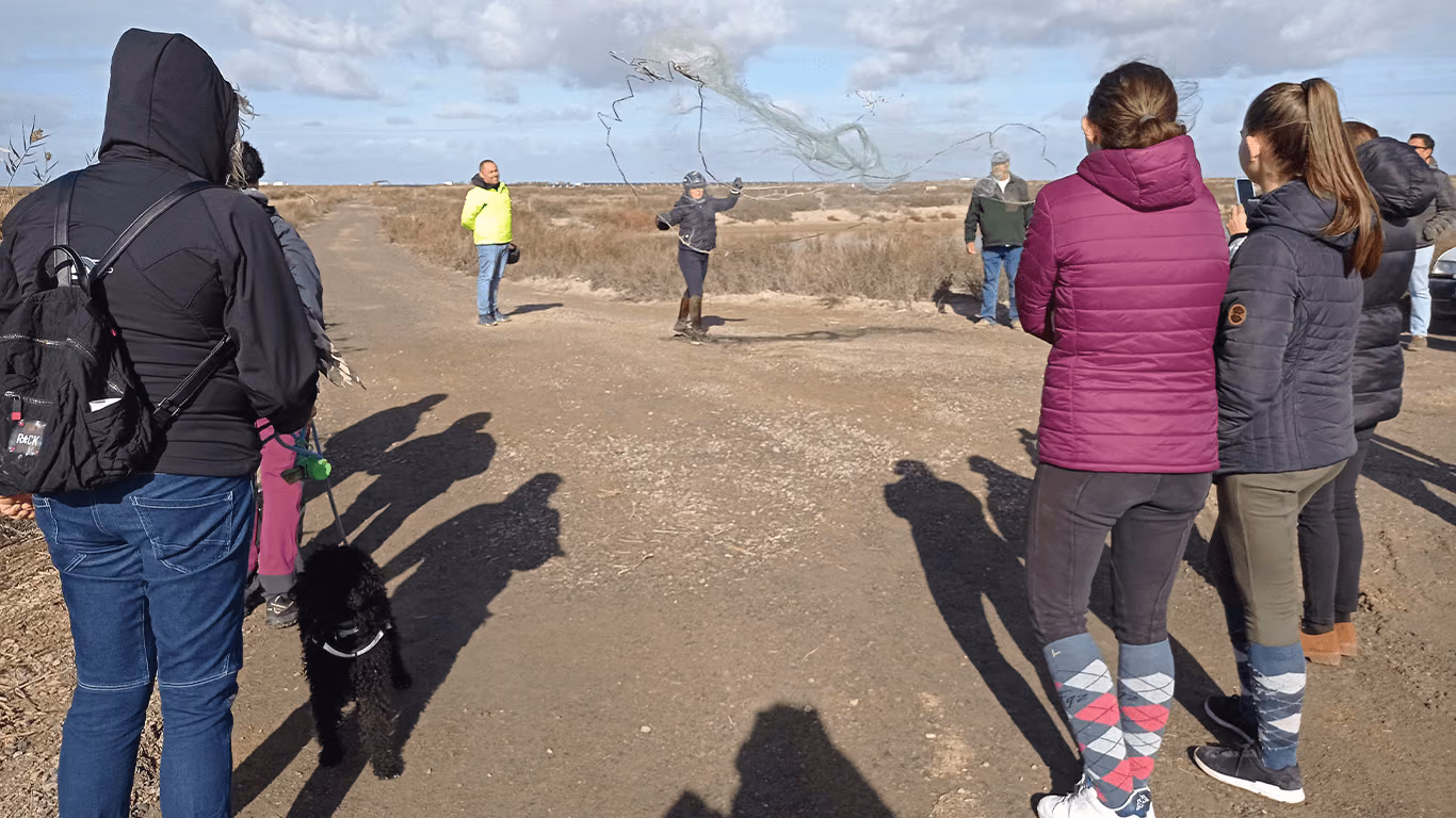 Visitantes observan la pesca con atarraya en un camino de la marisma
